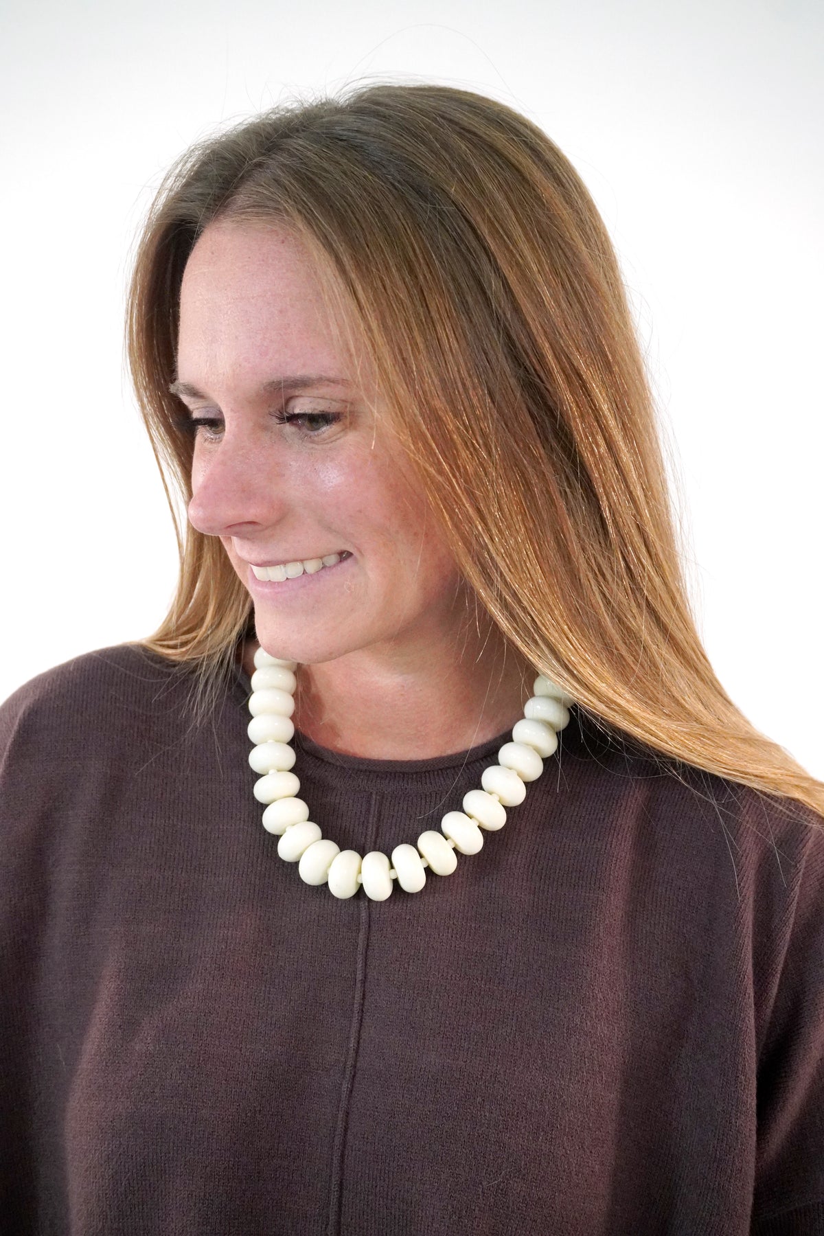 Chunky cream beaded collar necklace with large rondelle beads, worn over a brown crewneck knit sweater