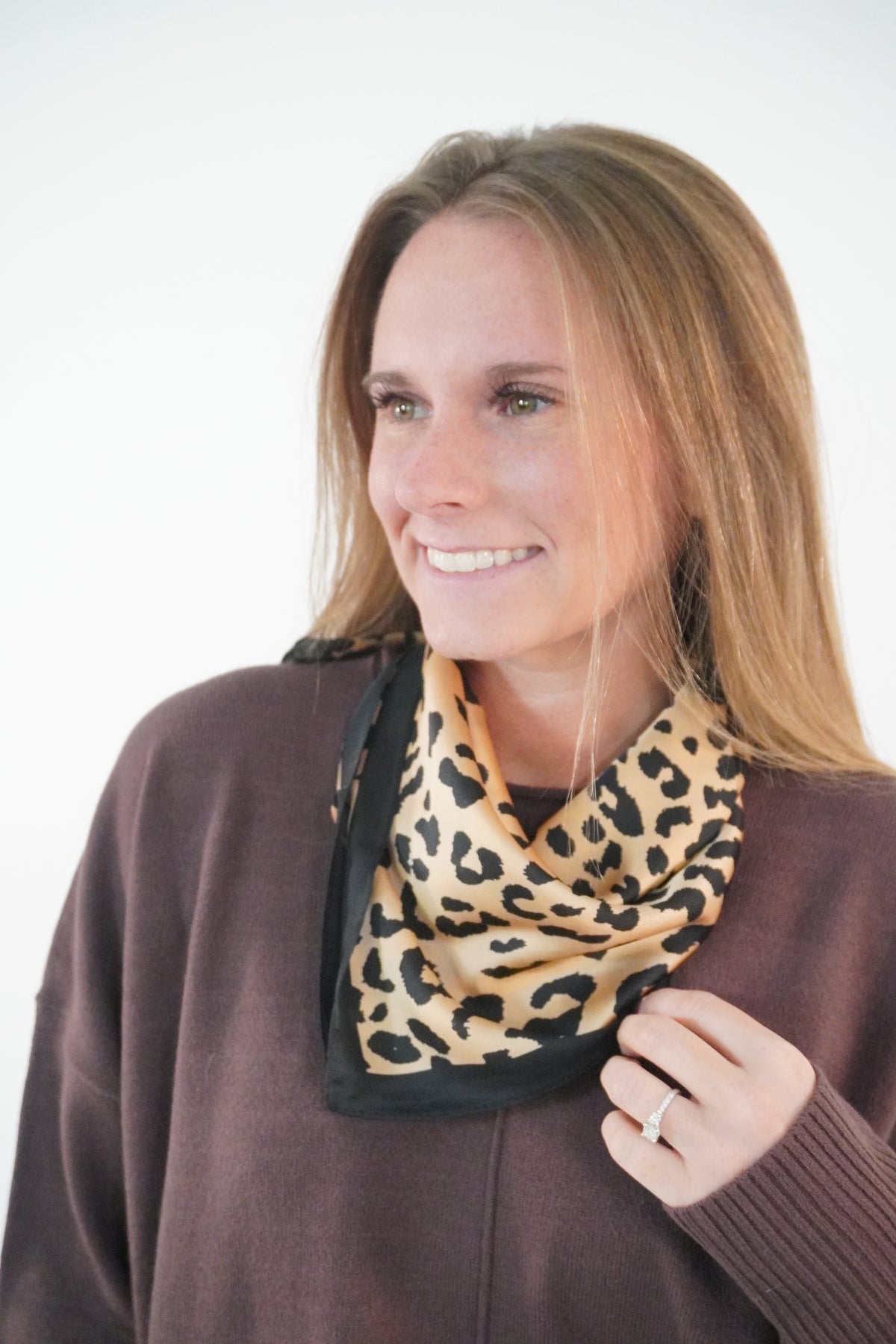 Leopard print satin square scarf with black border tied at the neck over a plum brown sweater