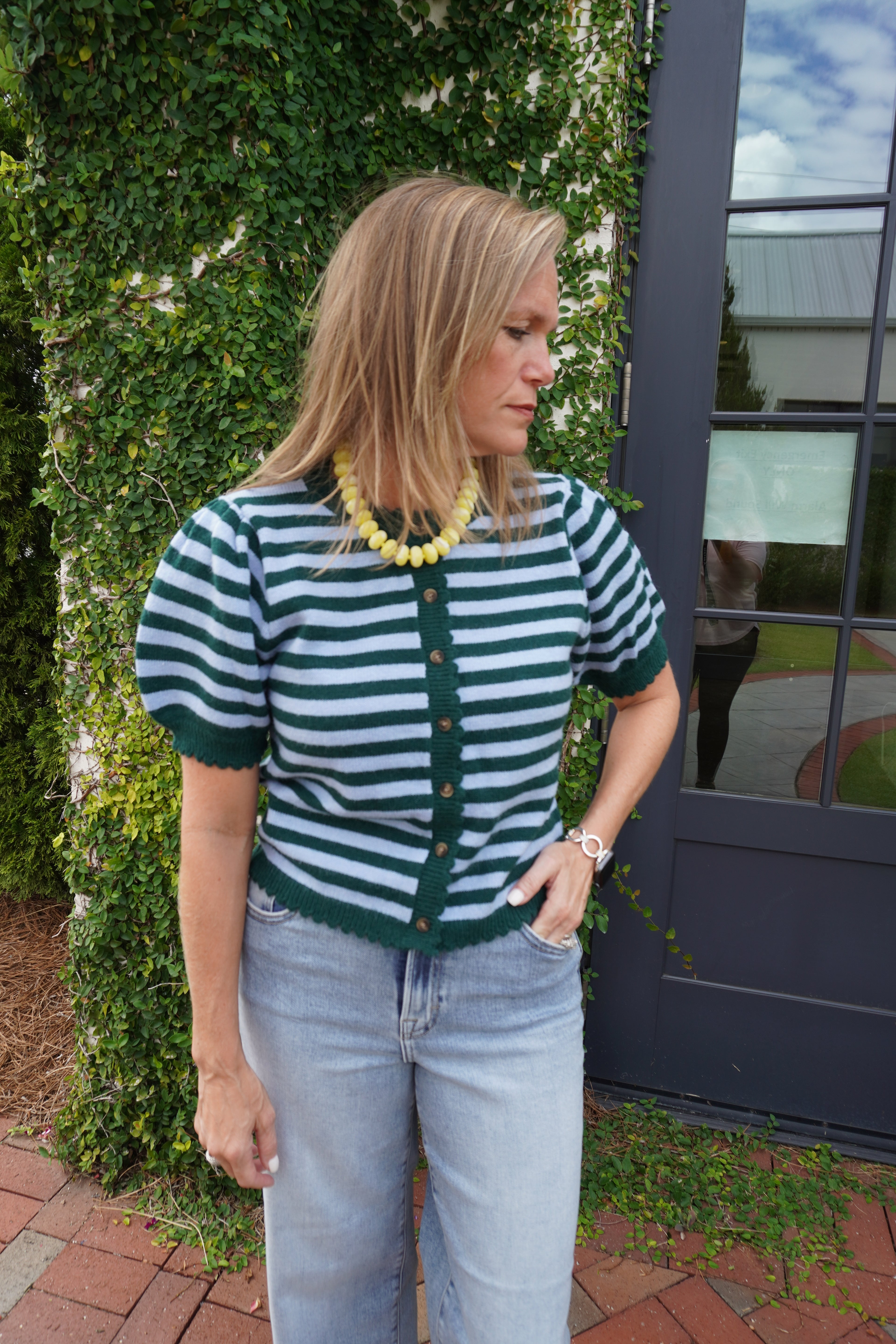 Woman wearing a green and light blue striped short sleeve button-front cardigan with puff sleeves and light wash jeans