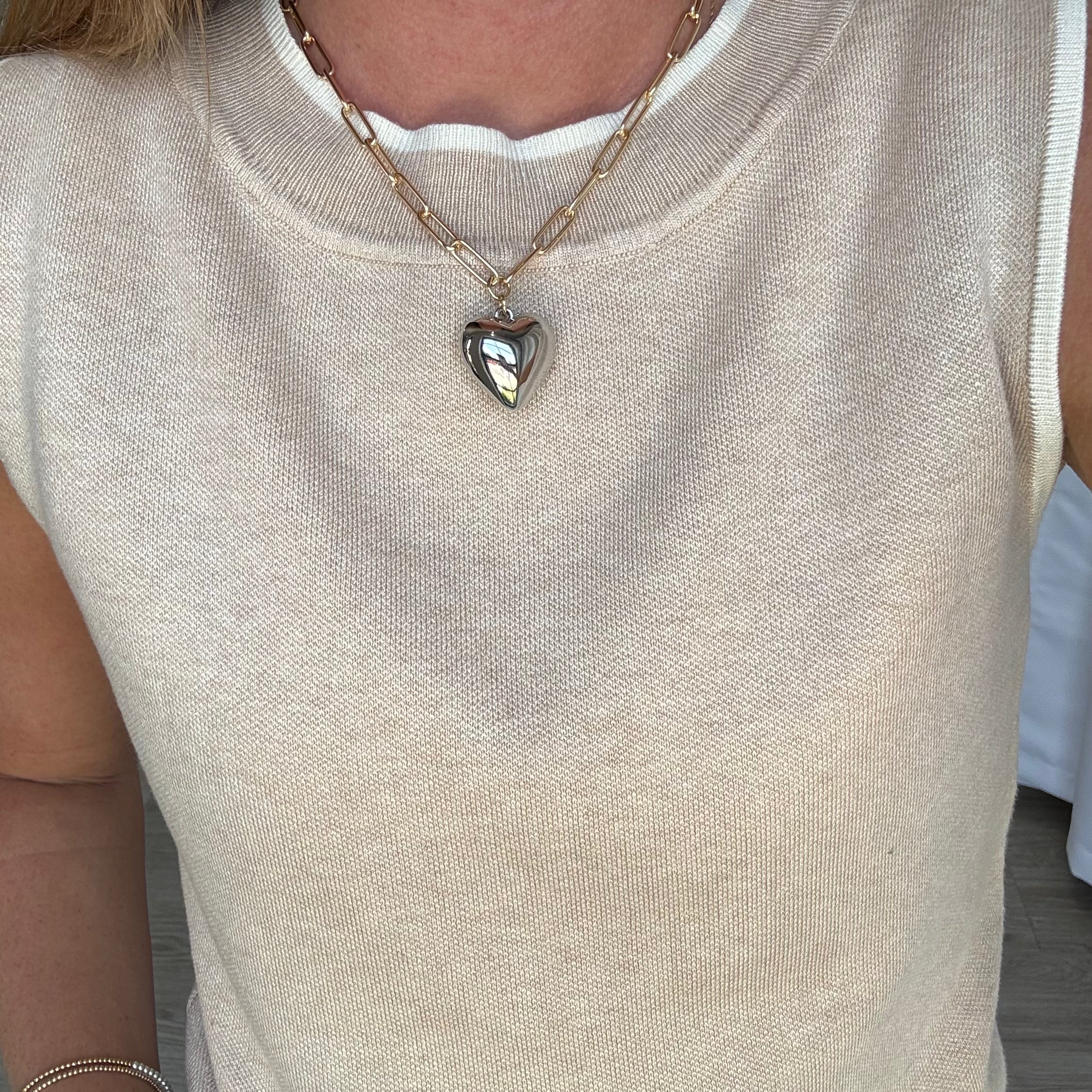 Person wearing a beige sleeveless top with a heart-shaped pendant necklace.
