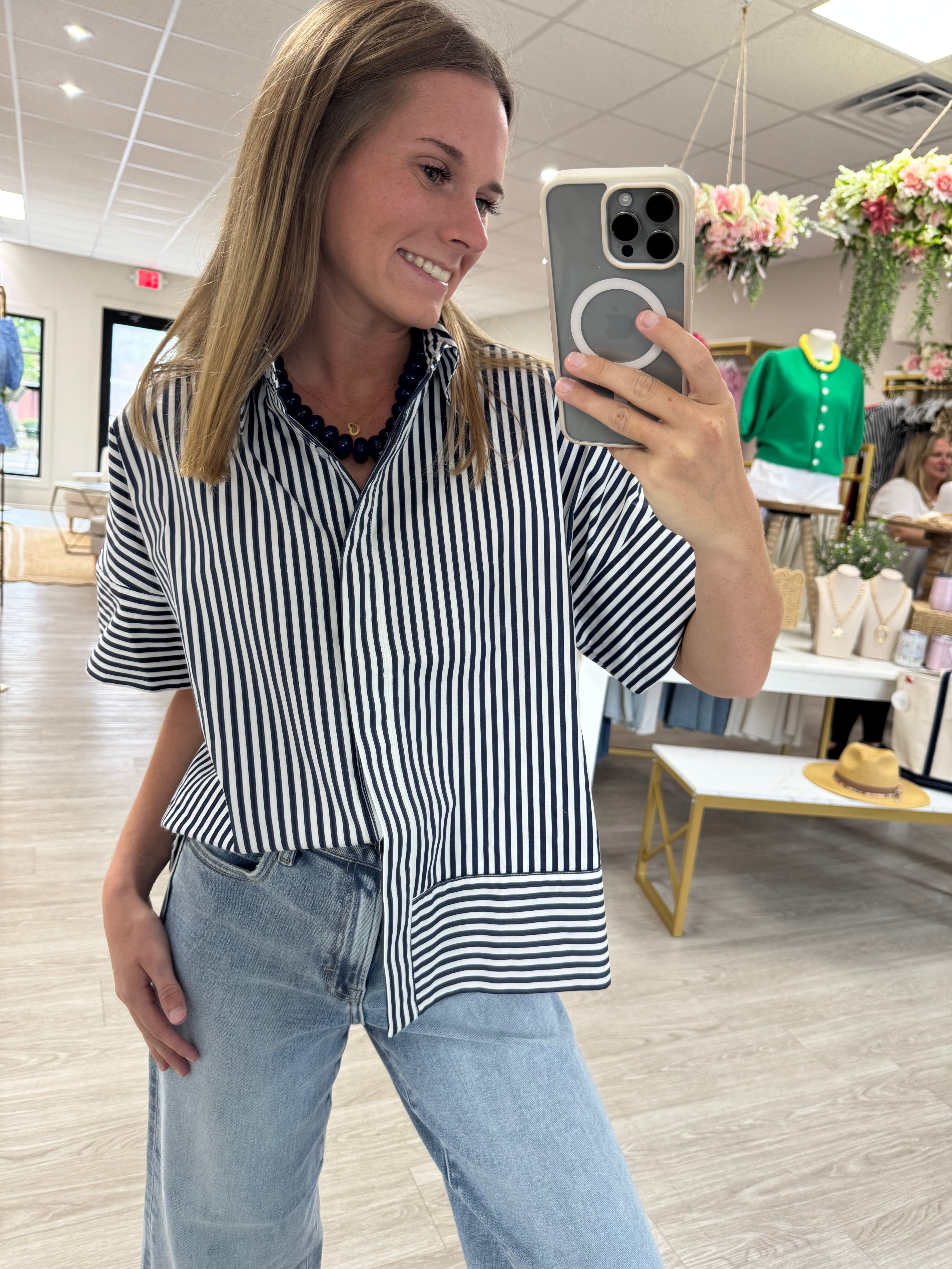 Navy and white striped short sleeve button-down blouse with a classic collar, mixed stripe detailing, and an oversized relaxed fit. Lightweight cotton top styled tucked into light wash wide-leg jeans for an effortless everyday look.
