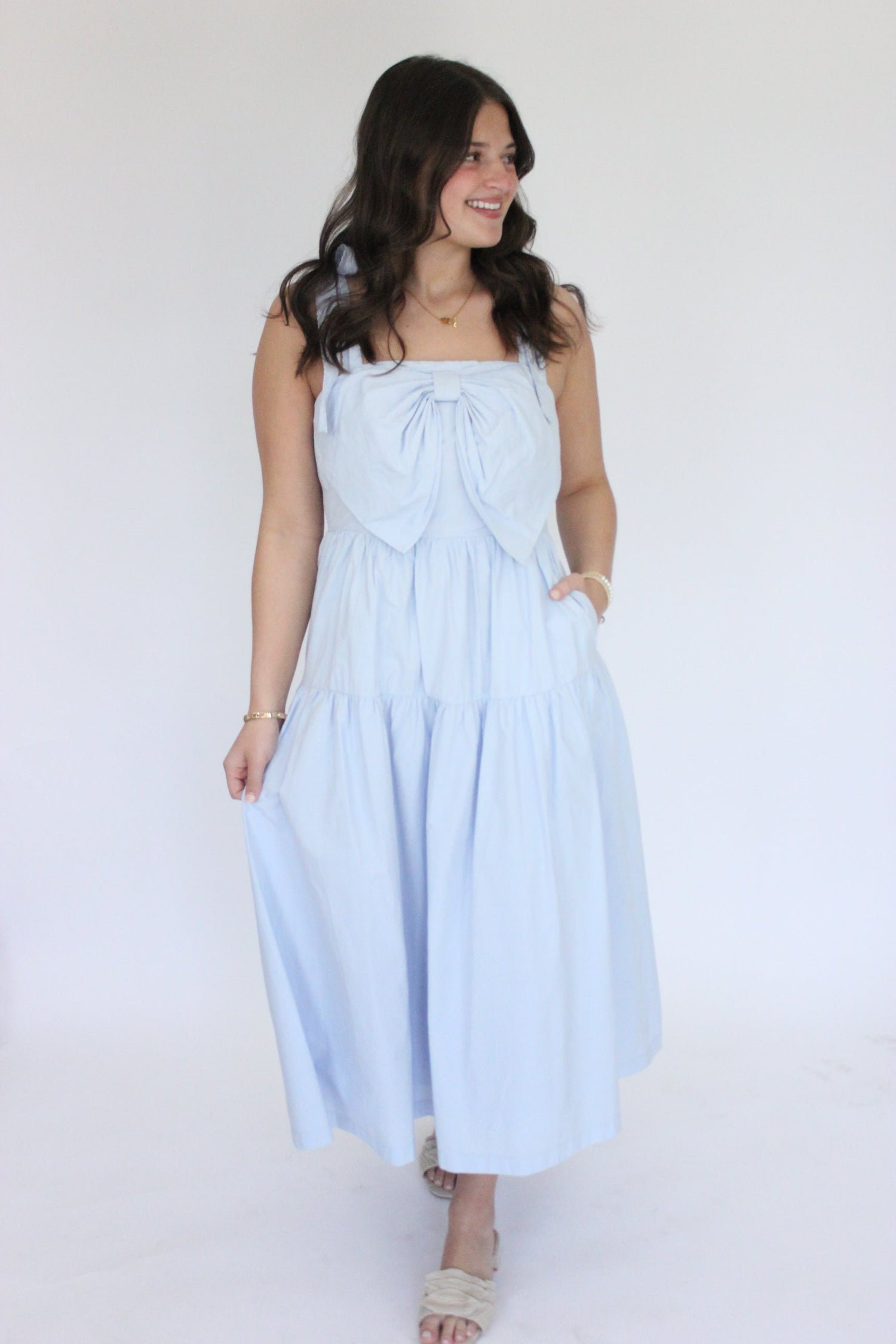 Woman in a light blue maxi dress with a bow detail, posing stylishly against a white backdrop. Perfect summer fashion inspiration