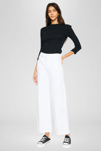 Cancun Jean-Woman wearing a black top and white pants on a plain background