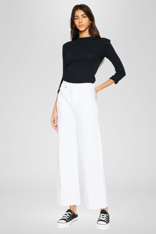 Cancun Jean-Woman wearing a black top and white pants on a plain background