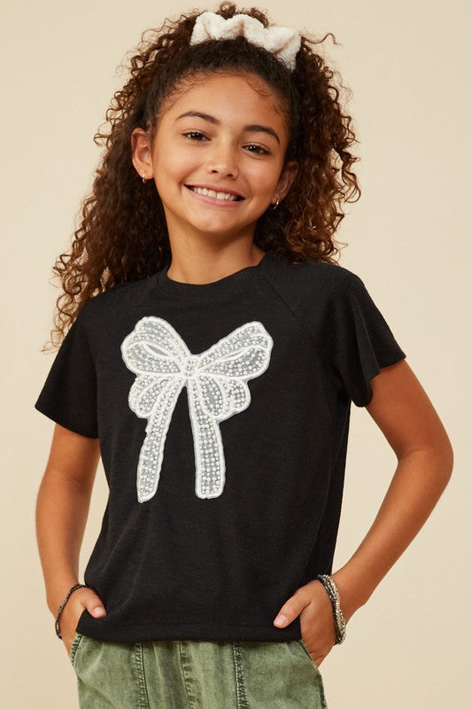 Young girl wearing a black t-shirt with a white bow design on a beige background