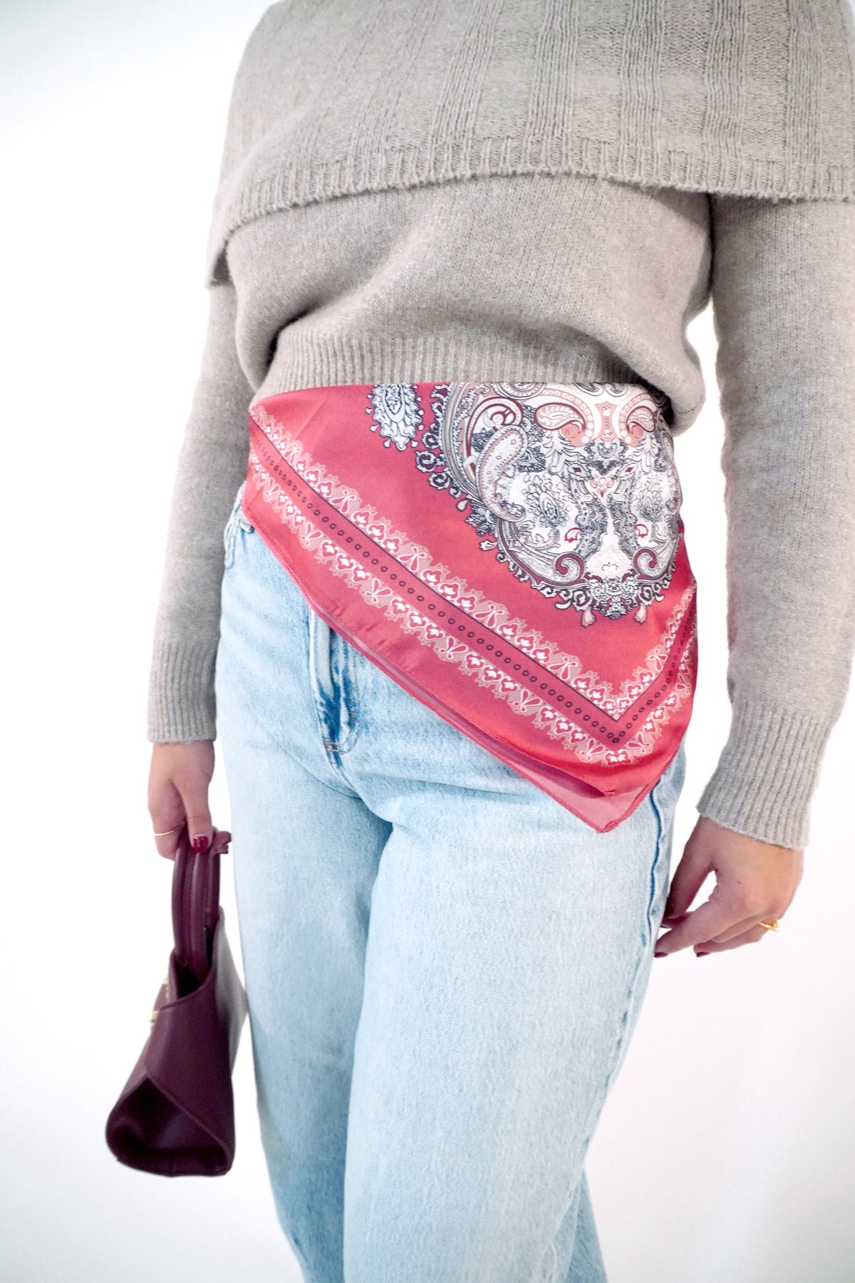 Coral red paisley print satin square scarf tied as a hip wrap over light wash jeans with a taupe sweater