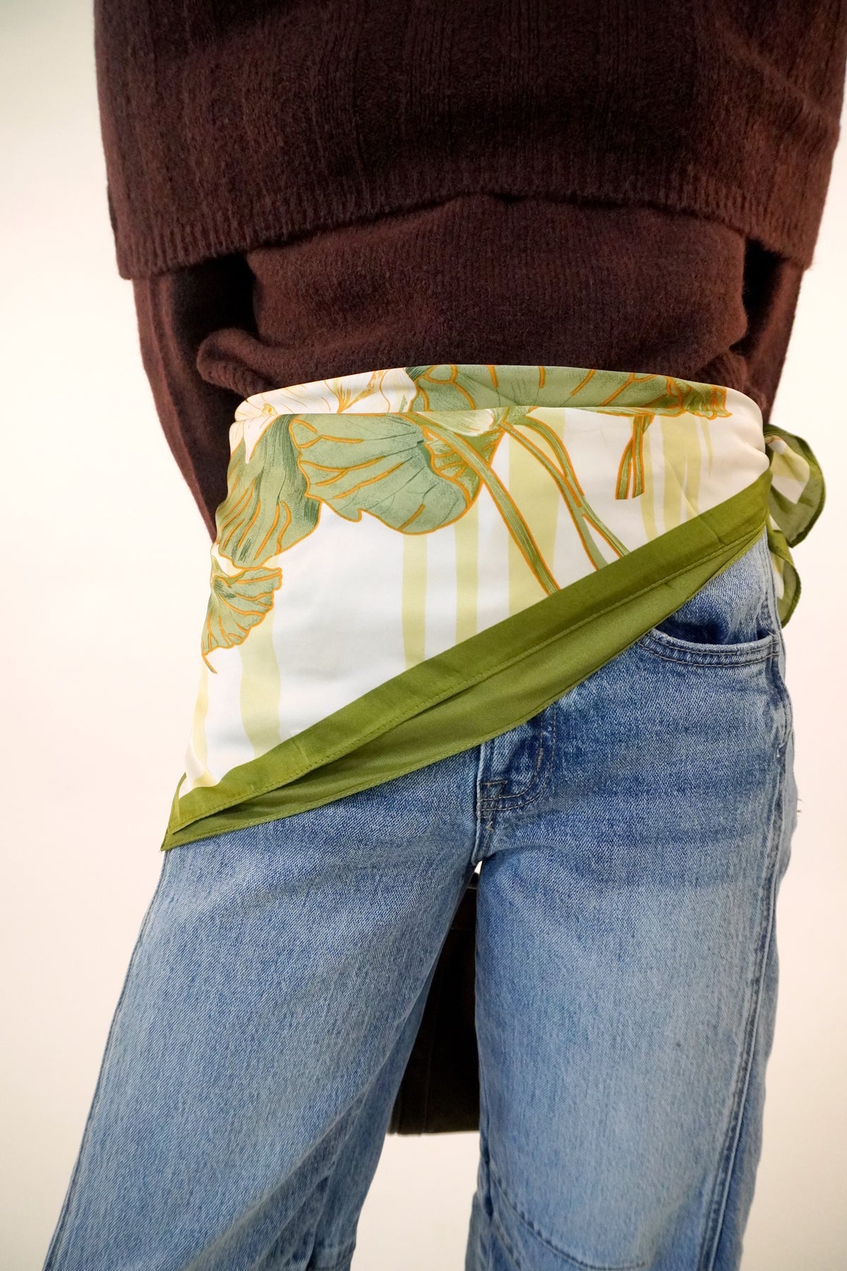 Green and cream lotus floral print satin square scarf tied as a hip wrap over jeans with a brown sweater