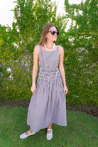 Woman wearing a brown and white gingham sleeveless midi dress with a fitted waist and full skirt