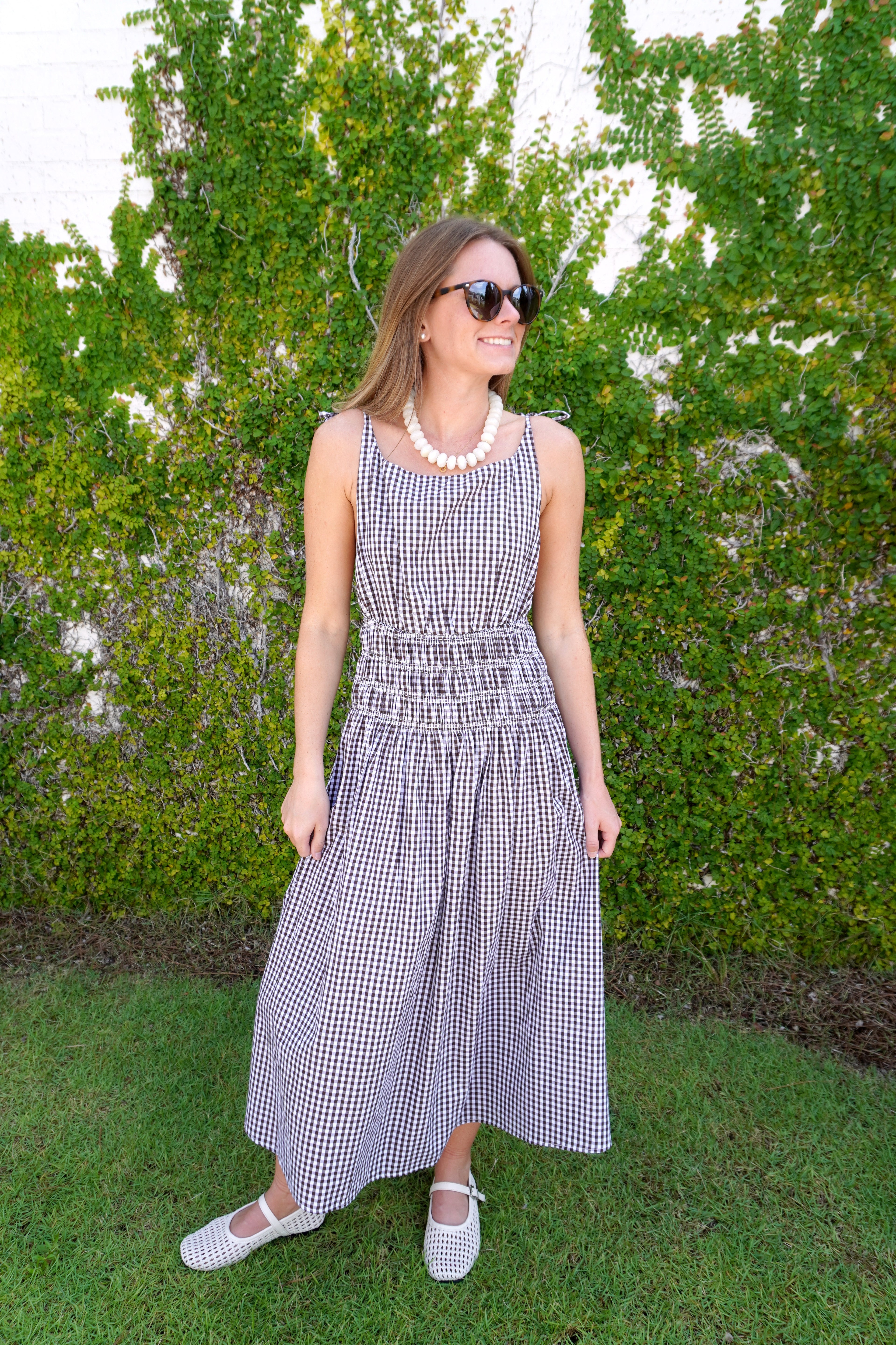 Woman wearing a brown and white gingham sleeveless midi dress with a fitted waist and full skirt