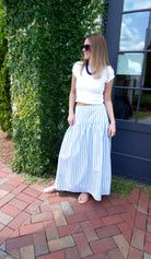 Woman wearing a white fitted short-sleeve top with a blue and white striped maxi skirt, navy statement necklace, and black sunglasses