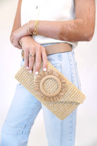 Natural woven straw crossbody clutch with gold chain strap and circular raffia detail, styled with a white top and light wash denim.