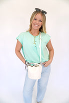 Cream textured mini bucket bag with top handle and detachable crossbody strap, styled with a mint green top and light wash denim.