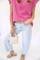 Cream woven mini handbag with structured top handle, styled with a pink short-sleeve blouse and light wash denim.