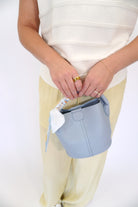 White oval clutch with oversized gold curved handle, styled with a soft yellow dress and layered gold bracelets.