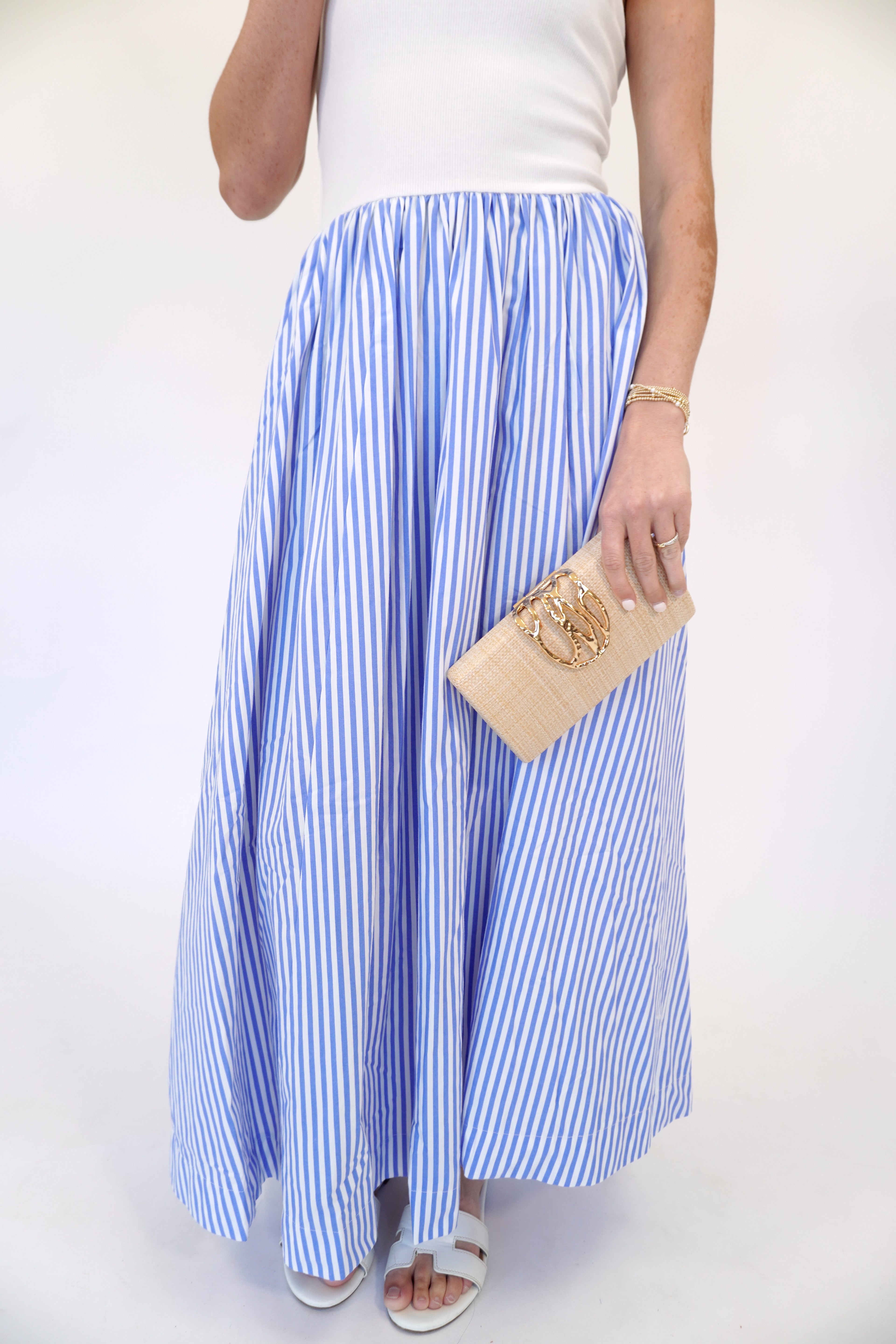 Blue and white striped strapless midi dress styled for spring and summer with white sandals, sunglasses, and gold clutch