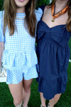 Two people wearing blue checkered and navy dresses on a grassy background