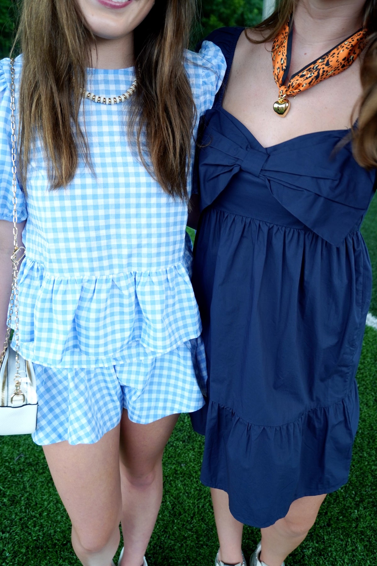 Two people wearing blue checkered and navy dresses on a grassy background