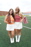Two women in cheerleading outfits with pom-poms on a sports field.