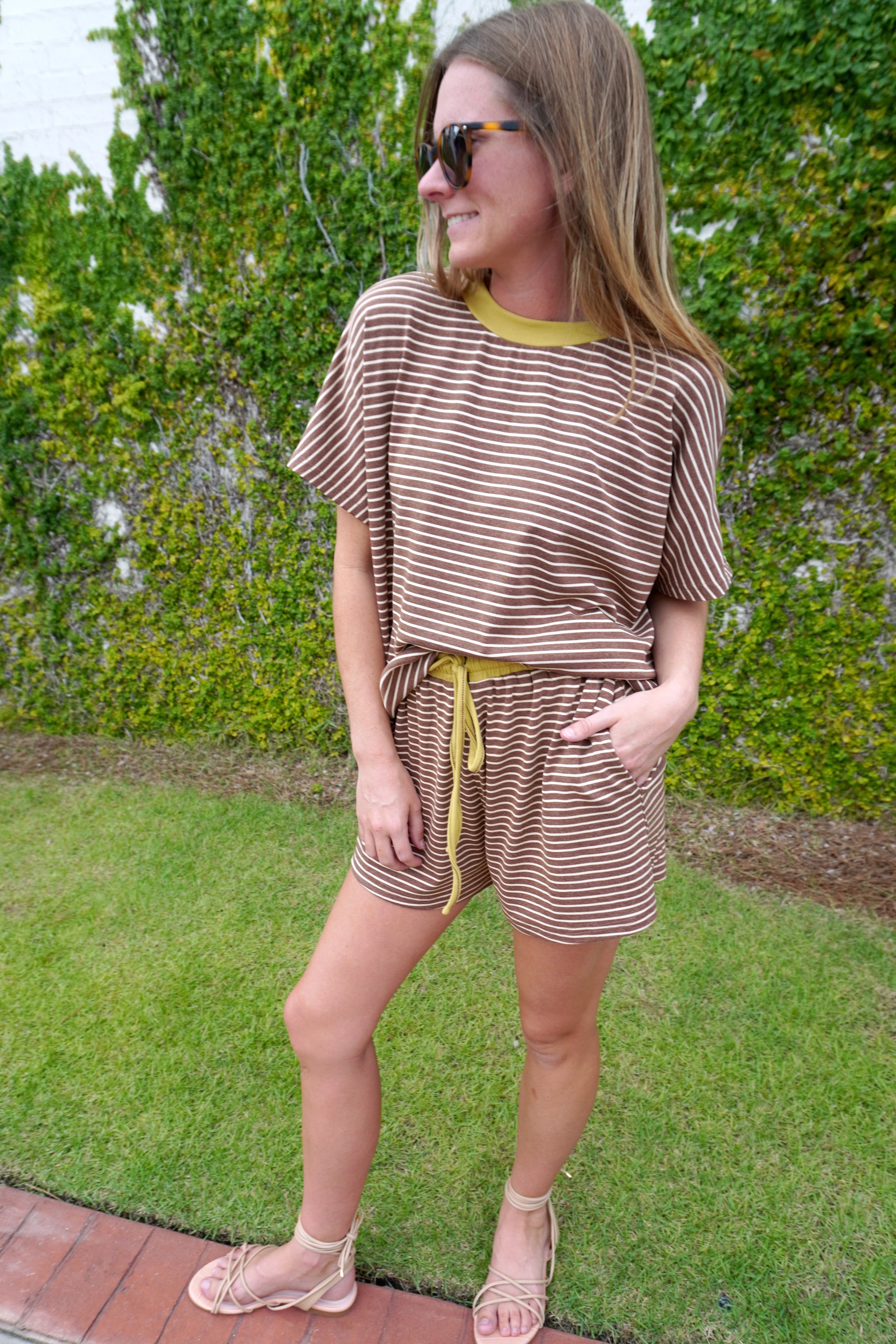 Woman wearing a brown and cream striped matching shorts set with mustard yellow trim and drawstring waist, styled with neutral sandals.