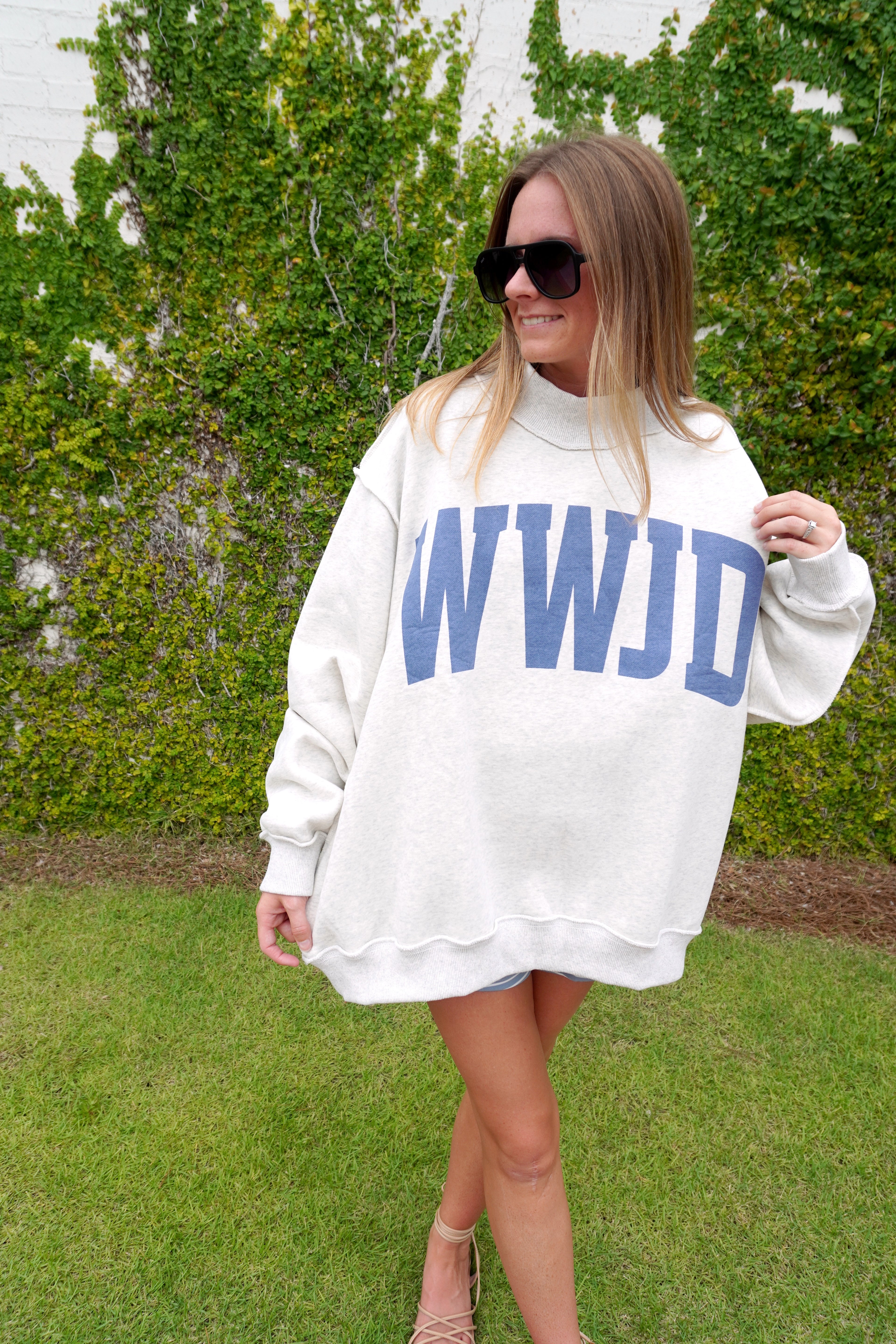 Woman wearing an oversized ivory sweatshirt with bold blue “AMEN” lettering, styled with shorts and sandals for a casual fall look.