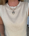 Person wearing a beige sleeveless top with a heart-shaped pendant necklace.
