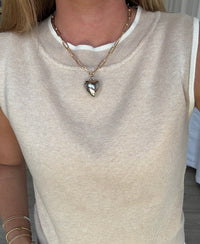 Person wearing a beige sleeveless top with a heart-shaped pendant necklace.