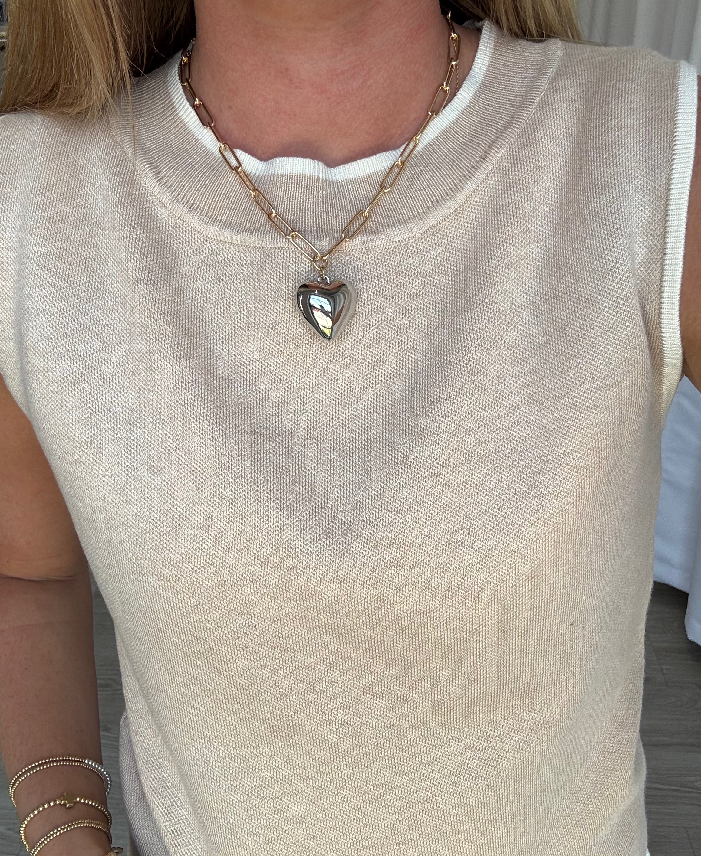 Person wearing a beige sleeveless top with a heart-shaped pendant necklace.