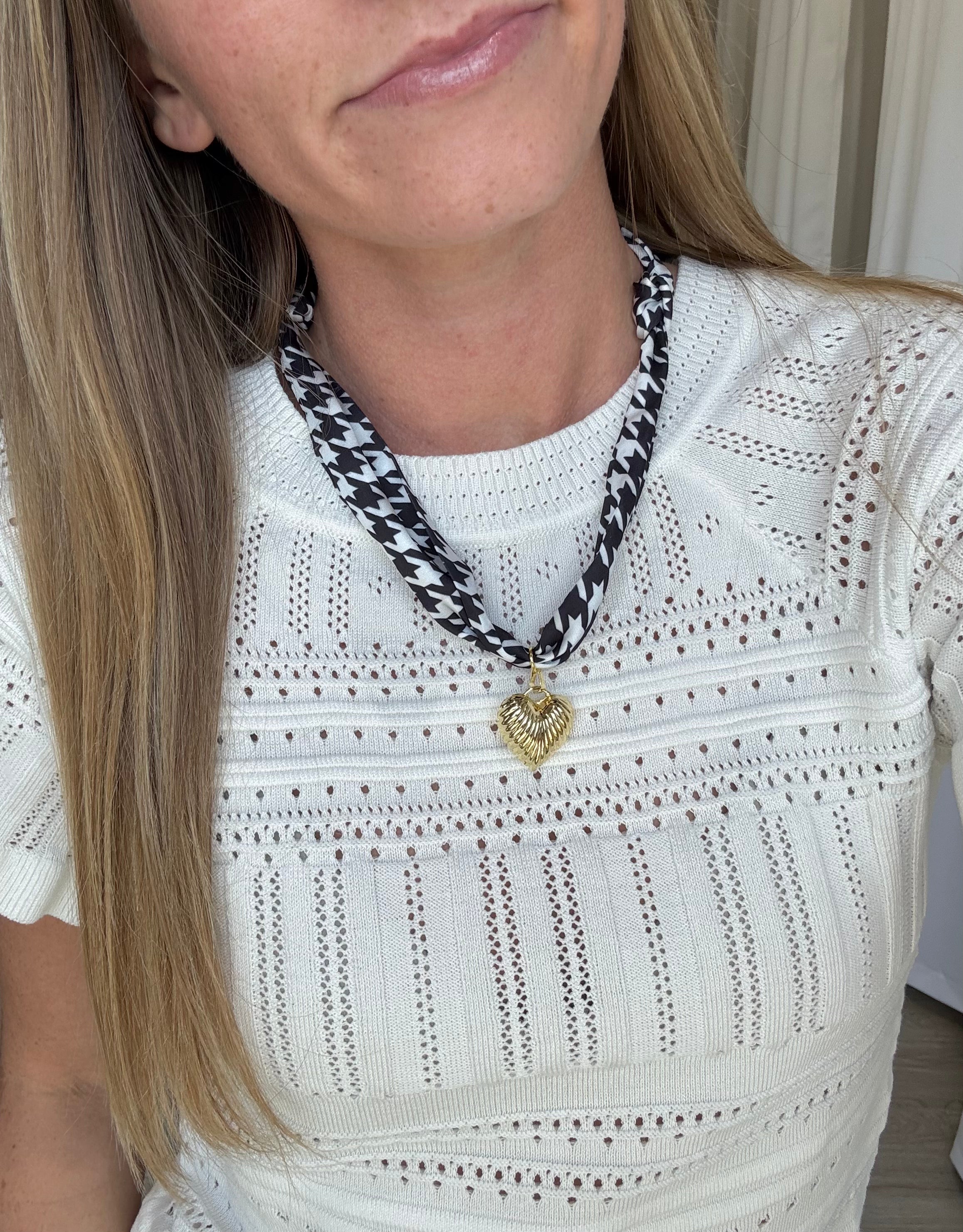 Black and white houndstooth scarf necklace featuring a gold heart pendant, styled around the neck for a chic, statement look