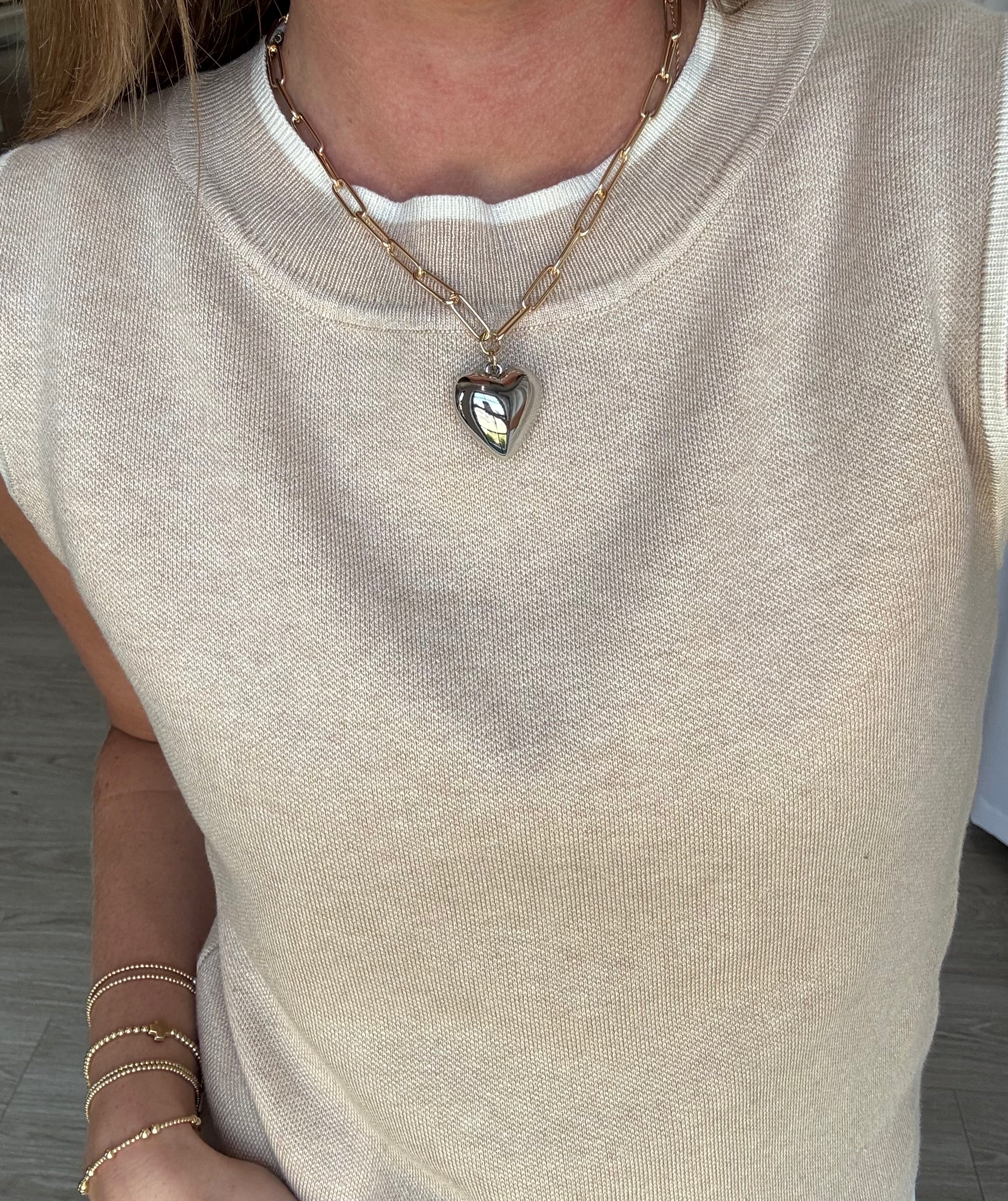 Person wearing a beige sleeveless top with a heart-shaped pendant necklace.
