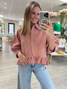 Dusty rose striped button-down peplum blouse with a collared neckline, chest pocket, three-quarter sleeves, and a relaxed fit. Lightweight woven top featuring vertical stripes and a feminine ruffle hem, perfect for pairing with denim for an effortless everyday look.