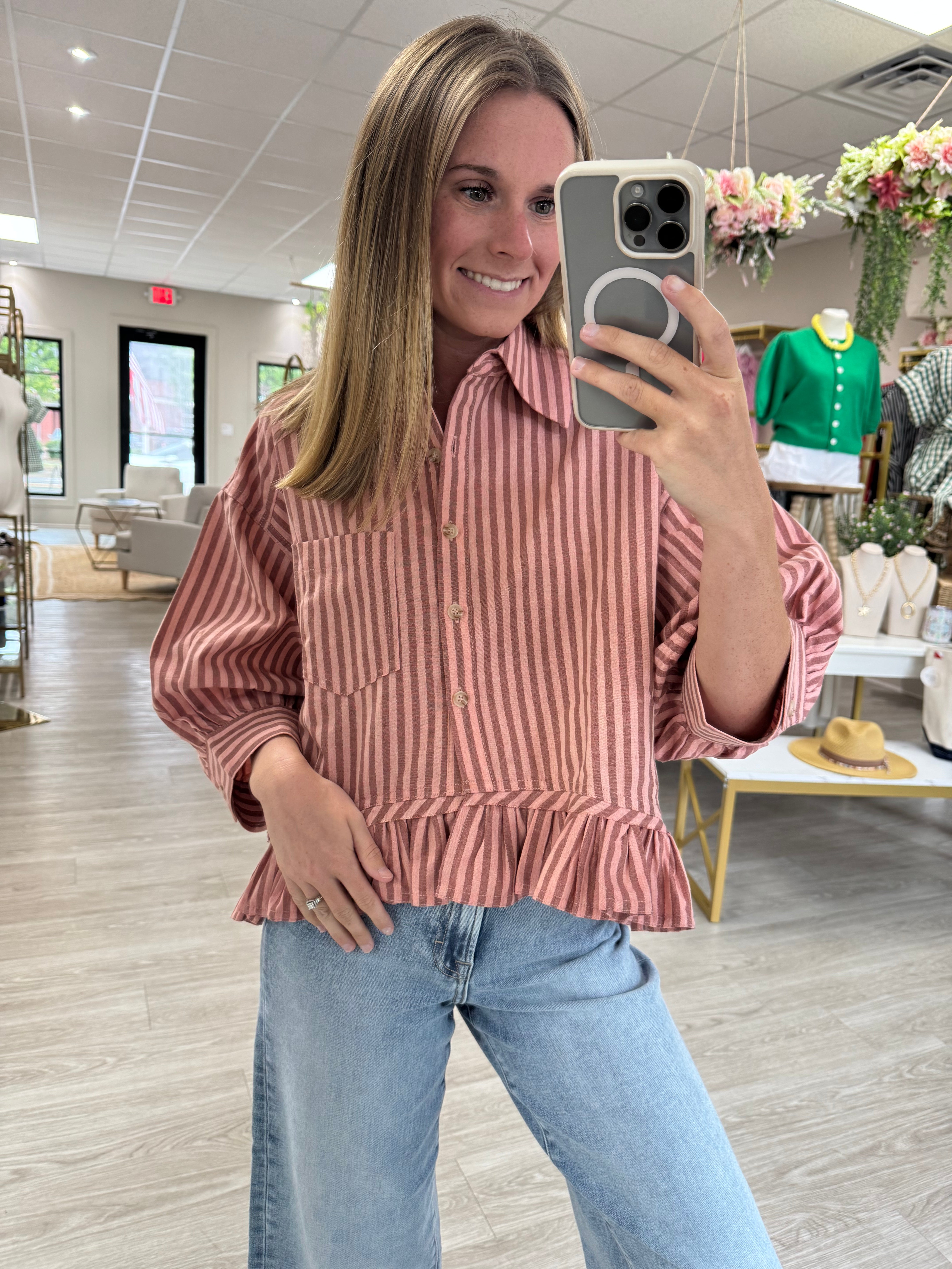 Dusty rose striped button-down peplum blouse with a collared neckline, chest pocket, three-quarter sleeves, and a relaxed fit. Lightweight woven top featuring vertical stripes and a feminine ruffle hem, perfect for pairing with denim for an effortless everyday look.