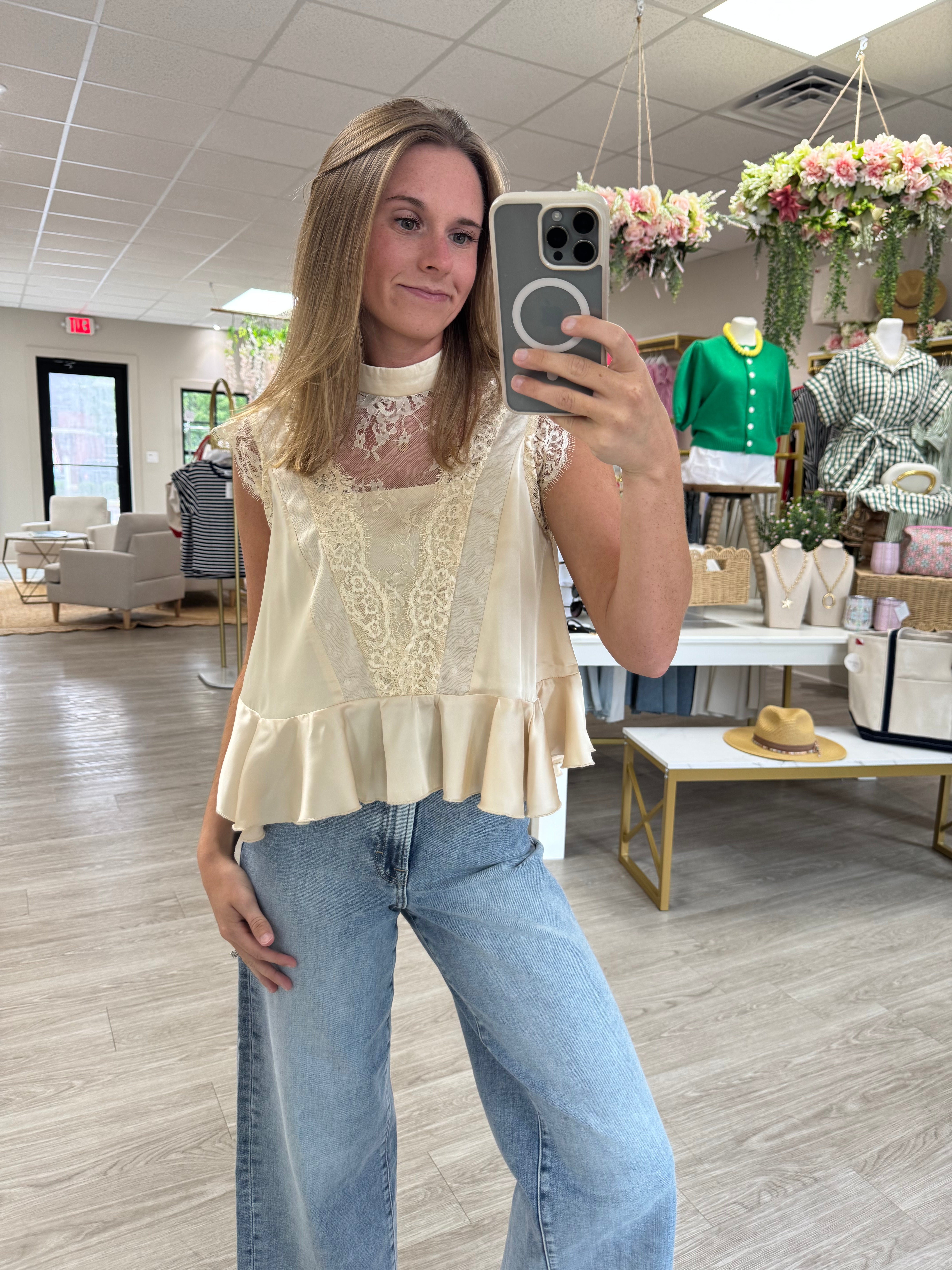 Cream sleeveless lace peplum blouse with a mock neckline, sheer floral lace yoke, intricate lace front panel, and soft ruffle hem. A feminine, romantic top perfect for pairing with denim or dress pants for effortless everyday style.