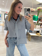 Navy and white striped short sleeve button-down blouse with a classic collar, mixed stripe detailing, and an oversized relaxed fit. Lightweight cotton top styled tucked into light wash wide-leg jeans for an effortless everyday look.