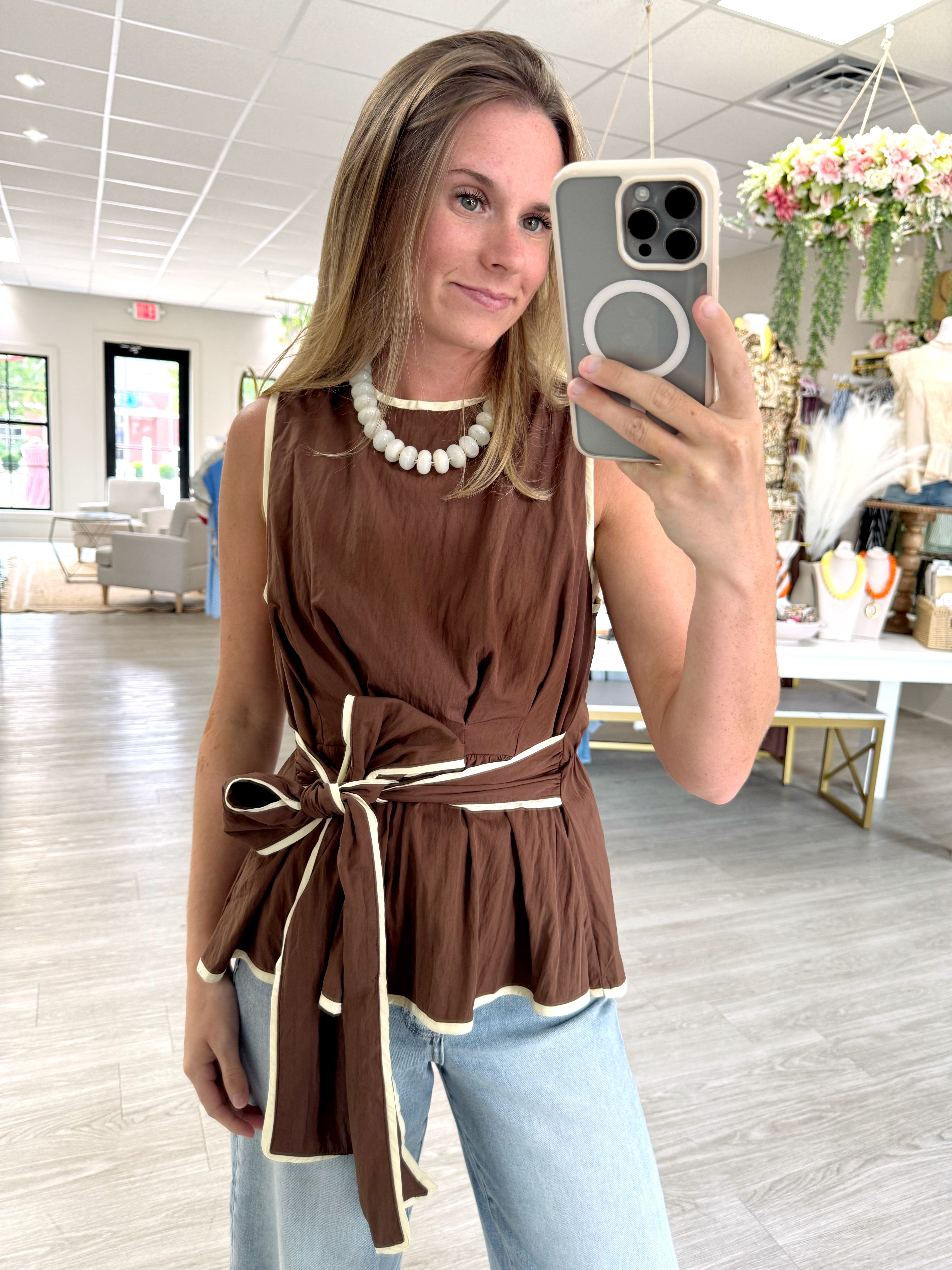 Brown sleeveless tie waist peplum top with cream contrast trim styled with light wash wide leg jeans
