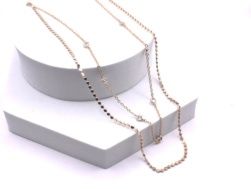 Two gold necklaces on a white stand with a white background